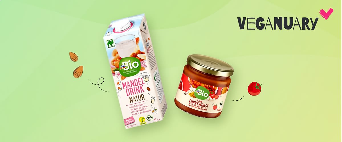 Ein Tetrapak mit der Aufschrift „Bio Mandeldrink Natur“ und ein Glas mit der Aufschrift „Bio Vegane Currywurst“ auf einem grünen Hintergrund. Links sind gezeichnete Mandeln und rechts eine Tomate. Oben rechts steht „Veganuary“ mit einem pinken Herz.