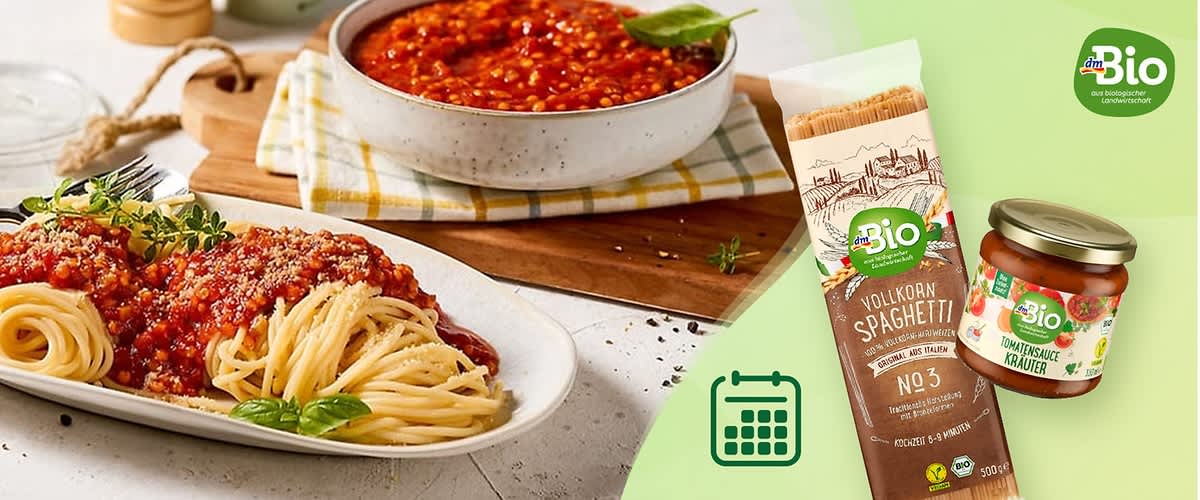 Eine Packung dmBio Vollkorn-Spaghetti neben einem Glas dmBio Tomatensauce Kräuter, im Hintergrund ein Teller mit Spaghetti und Tomatensauce