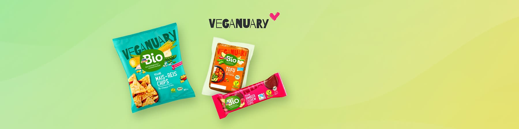 Eine Collage mit drei Produkten von dmBio vor einem grünen Hintergrund. Links eine Tüte vegane Mais-Reis-Chips, in der Mitte eine Packung Tofu, rechts ein veganer Proteinriegel. Oben rechts steht „Veganuary“ in schwarzer Schrift mit einem pinken Herz daneben.