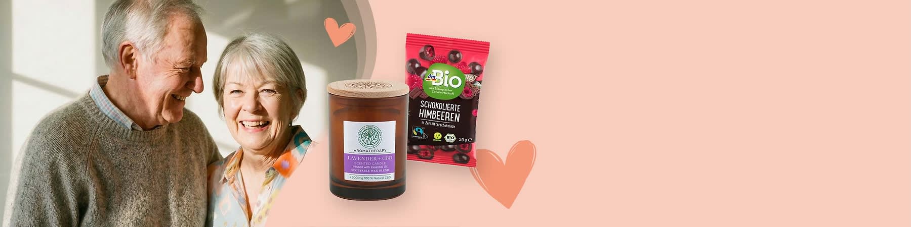 Eine braune Duftkerze mit der Aufschrift „Lavendel & Ceder“ und eine Packung Bio-Schokolierte Himbeeren mit grünem Bio-Logo auf einem beigen Hintergrund mit Herzsymbolen