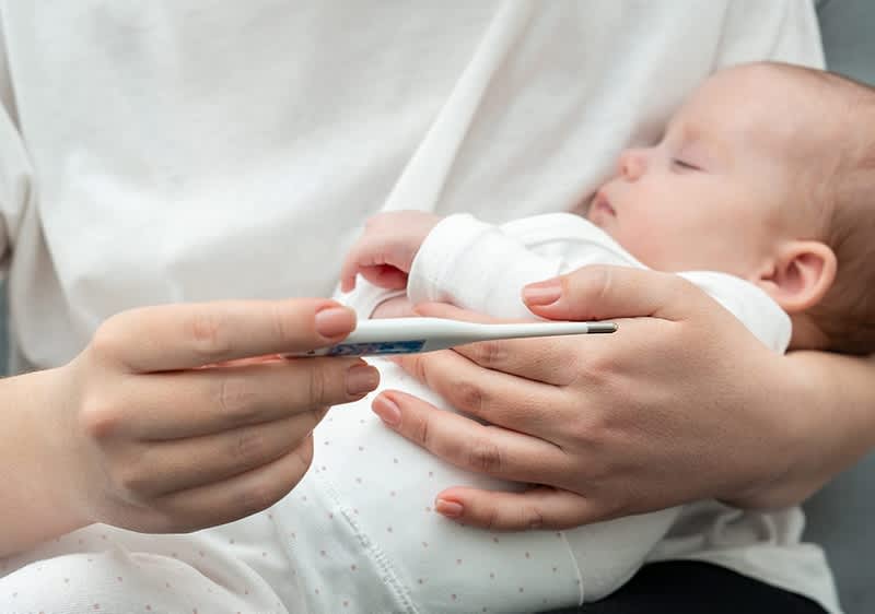 Frau hält Baby und Fieberthermometer