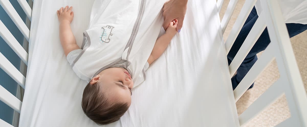 Erwachsener legt Baby ins Gitterbett