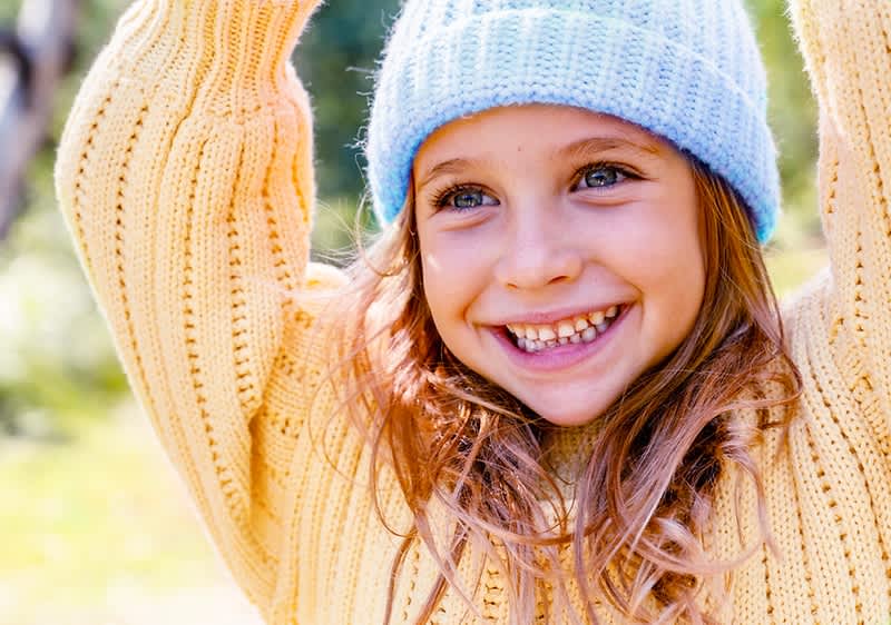 Eine Person in einem gelben Strickpullover und einer blauen Mütze hebt die Arme über den Kopf