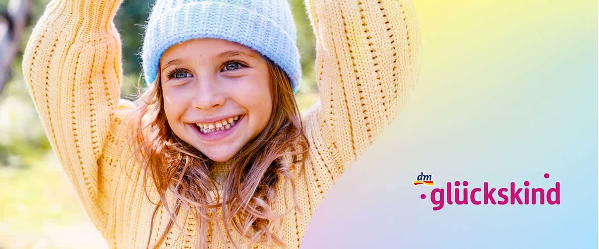 Eine Person in einem gelben Strickpullover und einer blauen Mütze hebt die Arme über den Kopf