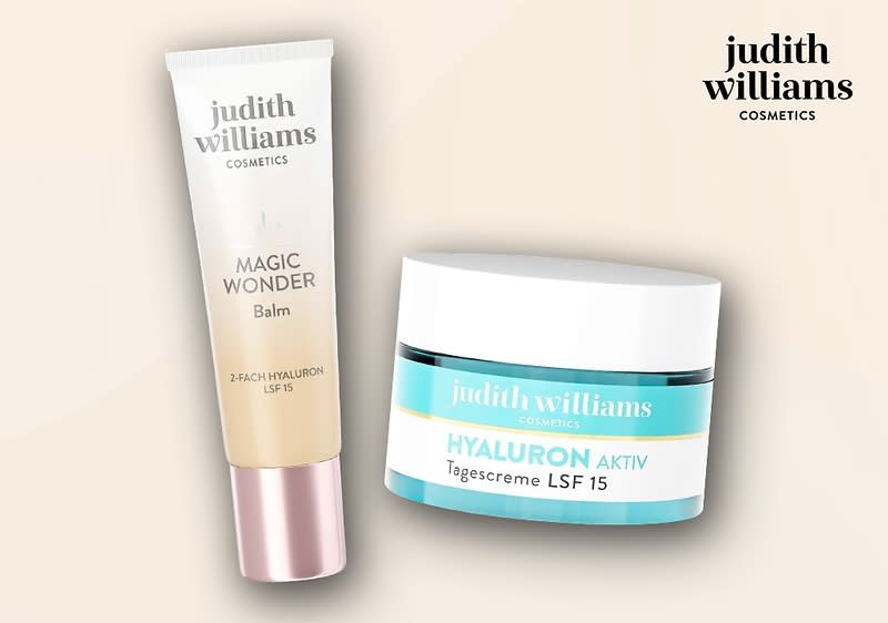 Zwei Produktverpackungen von Judith Williams Cosmetics, links ein Magic Wonder Balm in einer beigen Tube mit rosa Verschluss, rechts eine Hyaluron Aktiv Tagescreme LSF 15 in einem weißen Tiegel mit türkisfarbenem Etikett, oben rechts das Logo von Judith Williams Cosmetics