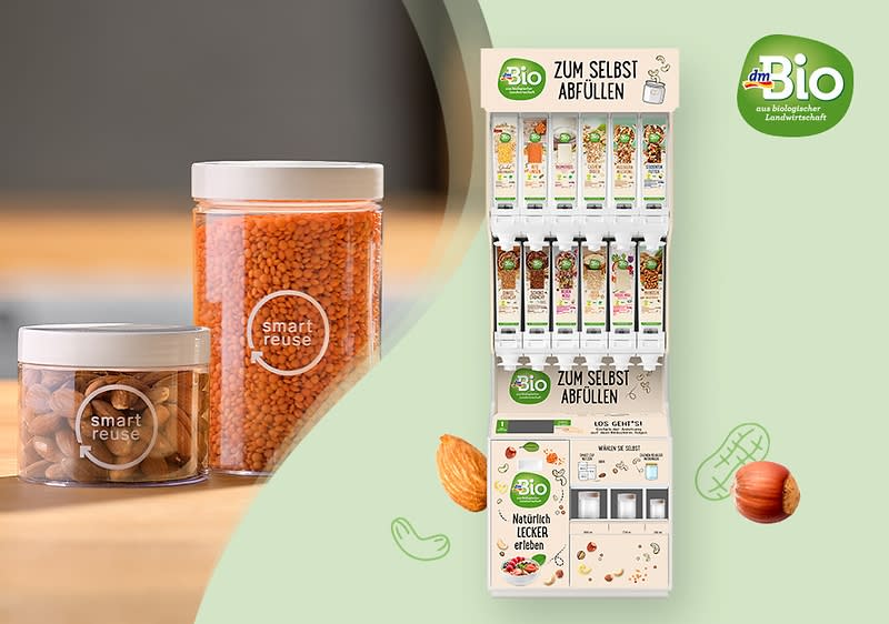 Zwei transparente Behälter mit der Aufschrift smart reuse enthalten rote Linsen und Mandeln, daneben eine Illustration einer dm-Abfüllstation mit der Aufschrift ZUM SELBST ABFÜLLEN, gefüllt mit verschiedenen Nüssen und Trockenfrüchten in Röhren, darüber das dmBio-Logo mit dem Slogan aus kontrolliert biologischem Anbau, umgeben von Illustrationen einer Mandel und einer Haselnuss sowie der Text dmBio Kurkuma Dicker Erbsen auf einer Verpackung.