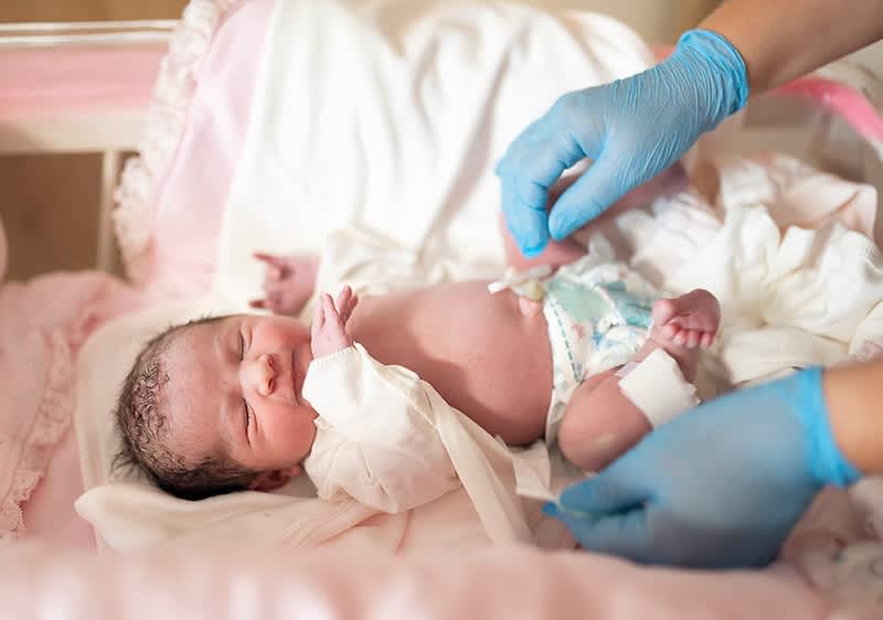 Neugeborenes wird von behandschuhter Hand versorgt