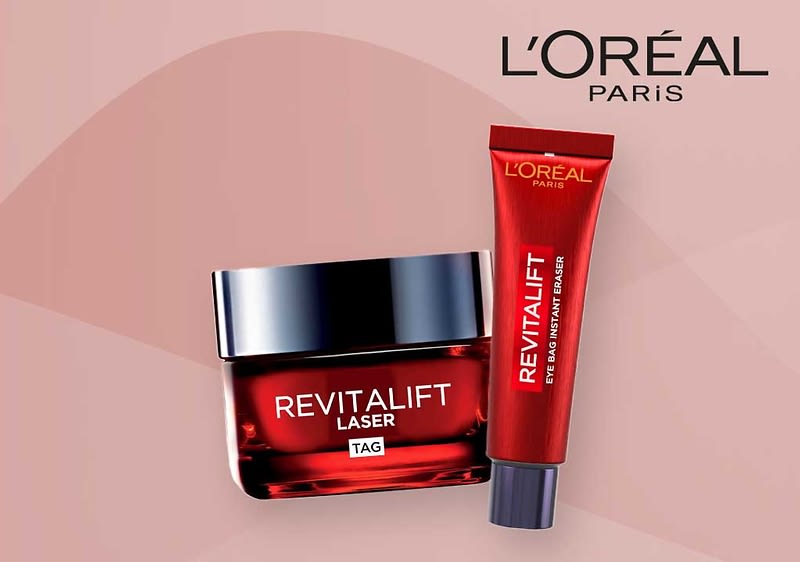 Zwei L'Oréal Paris Revitalift Produkte auf einem rosa Hintergrund, links eine rote Tube mit der Aufschrift Revitalift Eye Bag Instant Eraser und rechts ein quadratisches Glasgefäß mit schwarzem Deckel und der Aufschrift Revitalift Laser X3 Tag, oben rechts das L'Oréal Paris Logo