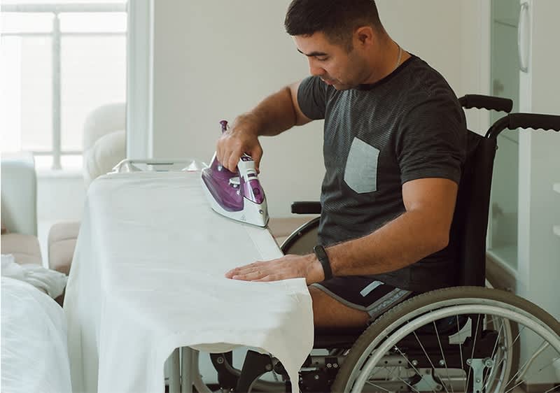 Mann im Rollstuhl bügelt Kleidung
