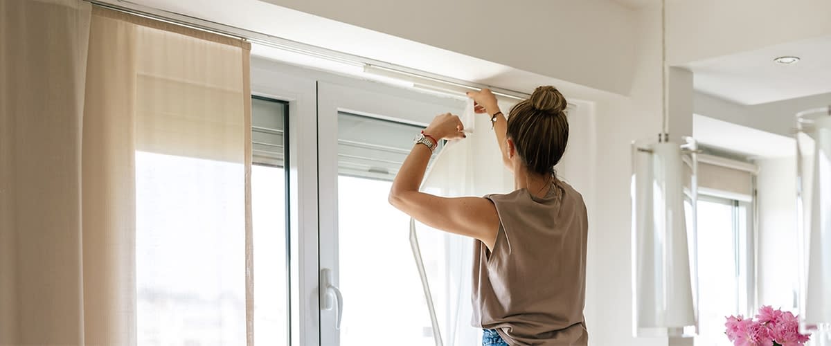 Frau hängt Vorhänge auf Fensterstange