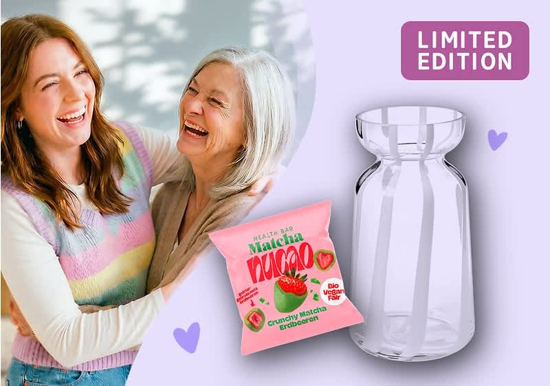 Zwei lächelnde Frauen in pastellfarbener Kleidung, nebeneinander stehend und sich umarmend, links ein rosa Snackbeutel mit der Aufschrift „MATCHA KINOKO“ und einer Erdbeerabbildung, rechts eine klare Glasvase und oben rechts ein lila Rechteck mit der Aufschrift „LIMITED EDITION“