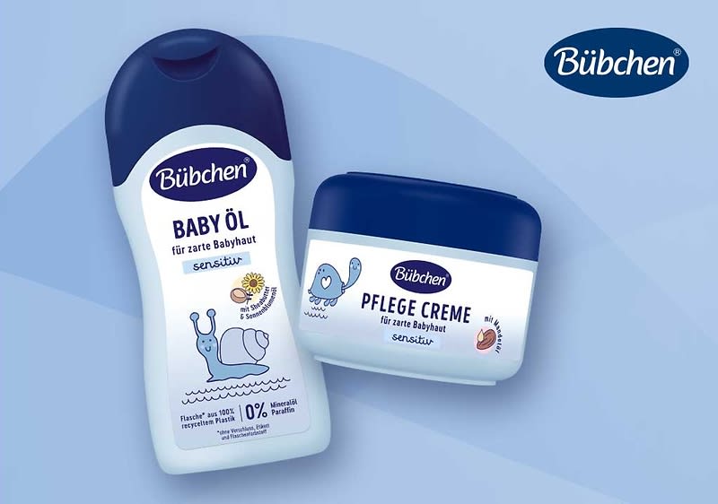 Zwei Bübchen-Babyprodukte vor blauem Hintergrund: links eine weiße Flasche mit dunkelblauem Deckel und Aufschrift „Bübchen Baby Öl für zarte Babyhaut sensitv“ mit Schnecken-Illustration, rechts eine weiße Dose mit dunkelblauem Deckel und Aufschrift „Bübchen Pflegecreme für zarte Babyhaut sensitiv“, oben rechts das Bübchen-Logo