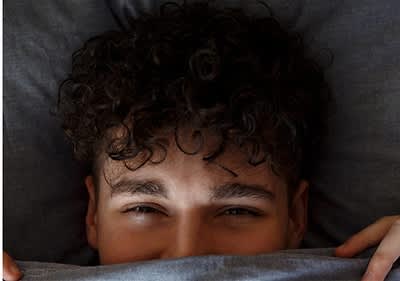 Mann mit lockigem Haar versteckt sich im Bett