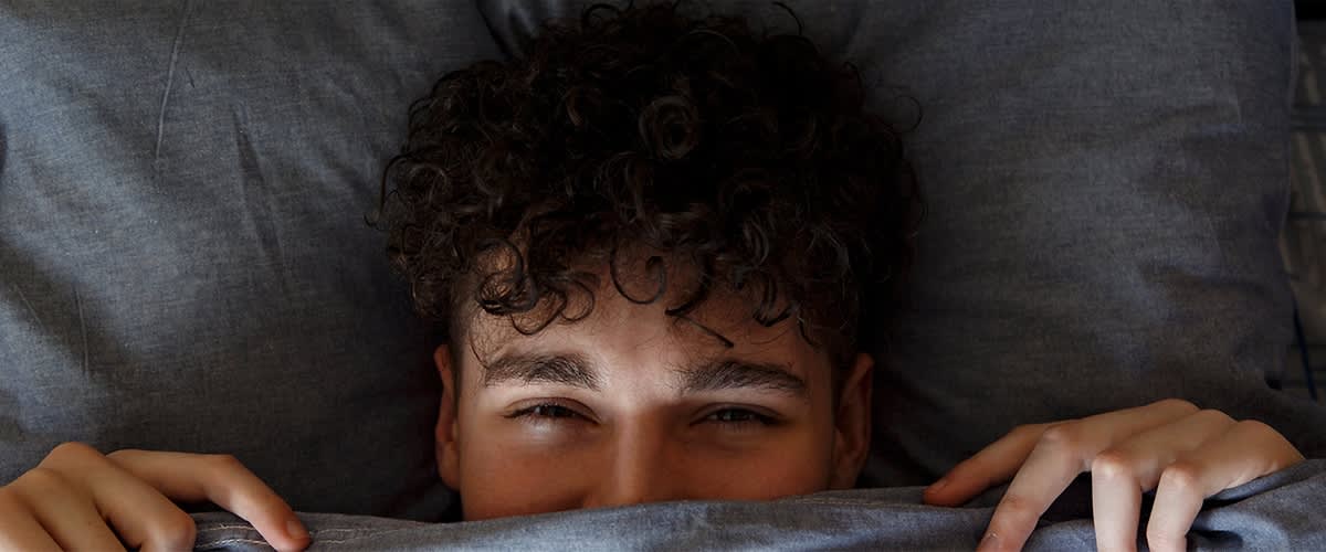 Mann mit lockigem Haar versteckt sich im Bett