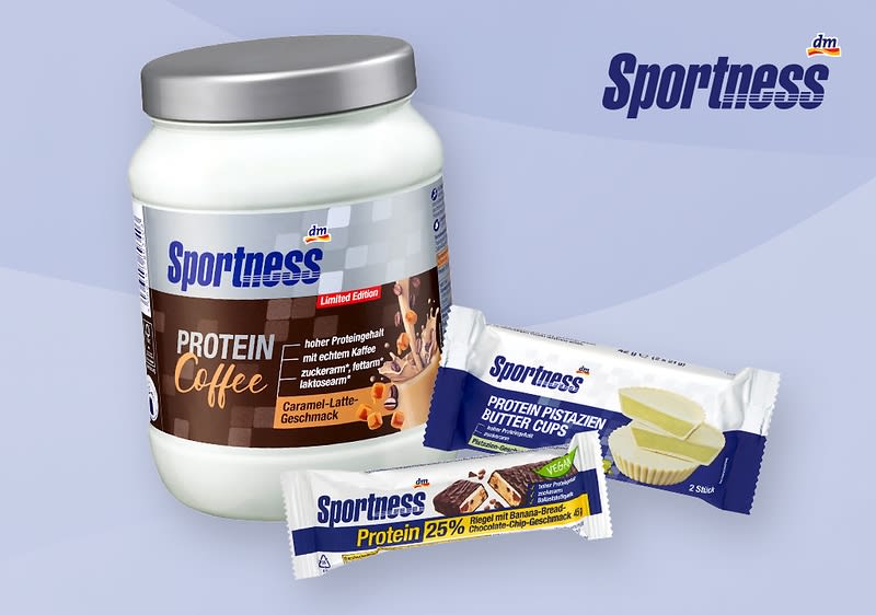 weiße Dose Sportness Protein Coffee mit silbernem Deckel und Aufschrift „Protein Coffee“ sowie zwei verpackte Sportness-Proteinsnacks nebeneinander, rechts ein weiß-blau verpackter Riegel mit Aufschrift „Protein 25%“ und oben ein weiß-blau verpackter Snack mit Aufschrift „Protein Pistazien Butter Cups“ auf hellblauem Hintergrund