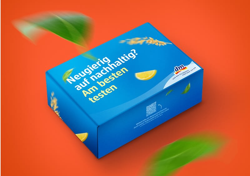 Bild mit orangefarbenem Hintergrund. In der Mitte ist eine blaue Box mit der Aufschrift „Neugierig auf nachhaltig? Am besten testen“ abgebildet.