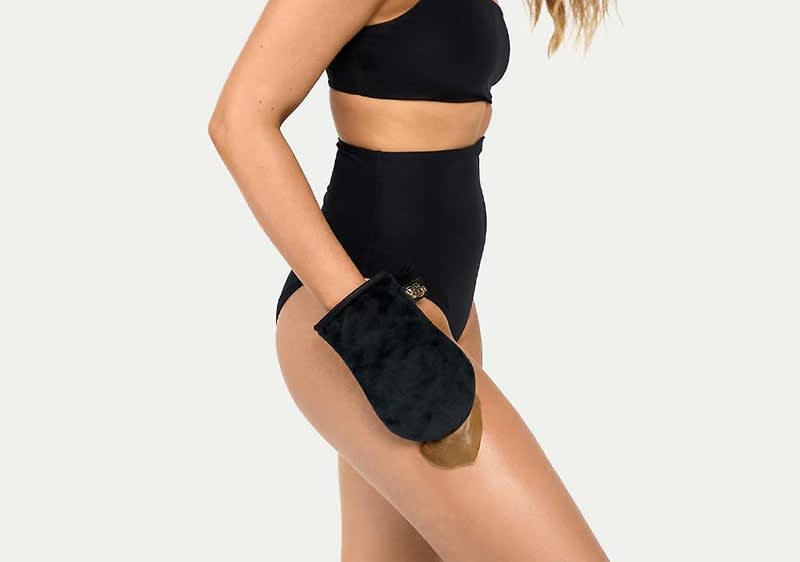 Seitlich abgebildeter Körper einer Frau von Brust bis Oberschenkel in schwarzem Bustier und hoch geschnittener schwarzer Unterhose, rechte Hand trägt einen schwarzen, pelzähnlichen Peeling-/Trockenbürstenhandschuh mit beige-braunem Innenfutter