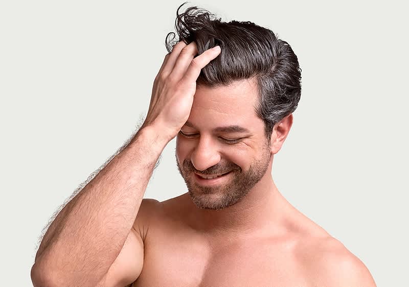 Mann berührt sein dunkelbraunes Haar mit Hand