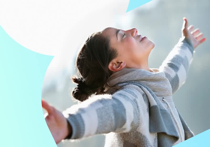 Eine Person in einem gestreiften Pullover und Schal breitet die Arme aus und steht vor einem hellen Hintergrund