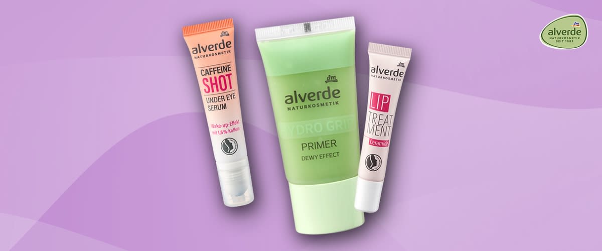 Drei Kosmetikprodukte von alverde vor lilafarbenem Hintergrund: links eine rosa Tube „CAFFEINE SHOT UNDER EYE SERUM“, mittig eine grüne Tube „alverde NATURKOSMETIK HYDRO GRE PRIMER DEWY EFFECT“, rechts eine hellrosa Tube „alverde LIP TREATMENT“ sowie oben rechts das runde alverde-Logo