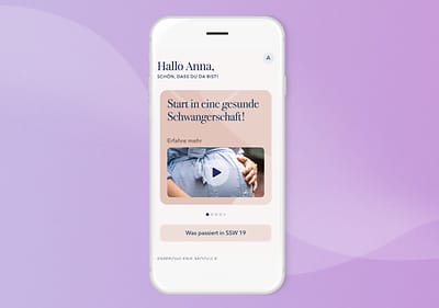 Ein Smartphone mit weißem Gehäuse zeigt auf dem Bildschirm die App Fertia mit einem lila Hintergrund, oben steht Hallo Anna, schön, dass du da bist!, darunter ein Bild von einer schwangeren Frau, die ihren Bauch hält, mit dem Text Start in eine gesunde Schwangerschaft! und einem Play-Symbol, darunter ein Button mit der Aufschrift Was passiert in SSW 19 und am unteren Rand steht Erfahrene Mütter antworten
