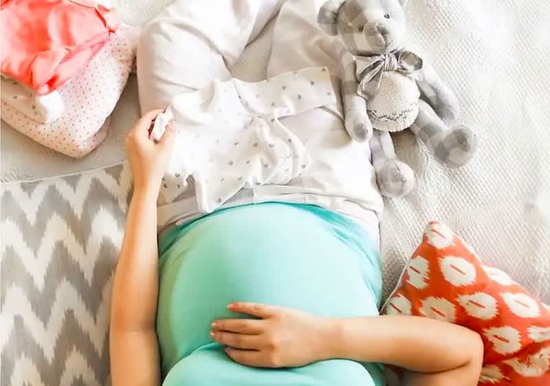 Schwangere Frau ordnet Babyerstausstattung