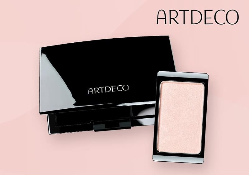 Eine schwarze, glänzende Puderdose mit dem weißen Schriftzug ARTDECO auf dem Deckel liegt geöffnet auf einem rosa Hintergrund, daneben befindet sich ein rechteckiger, heller Lidschatten in einer schwarzen Umrandung, oben rechts steht ebenfalls der Schriftzug ARTDECO in schwarzer Schrift.