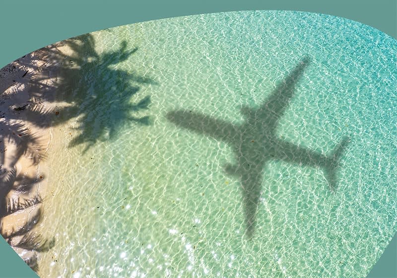 Ein Flugzeug wirft einen Schatten auf das türkisfarbene, klare Wasser eines Strandes, während die Sonne die Wellen glitzern lässt und die Silhouette von Palmen am sandigen Ufer sichtbar ist