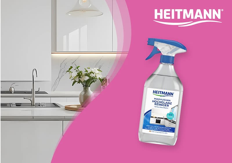 Eine moderne Küche mit weißer Einrichtung und einem silbernen Wasserhahn, daneben steht eine Vase mit grünen Pflanzen auf der Arbeitsplatte, rechts im Bild eine Produktverpackung des Heitmann Hochglanz-Reinigers mit blauem Sprühkopf, auf der Verpackung steht Heitmann und Hochglanz Reiniger sowie ein Bild einer glänzenden Küchenoberfläche, oben rechts der Schriftzug HEITMANN in Weiß auf türkisfarbenem Hintergrund.