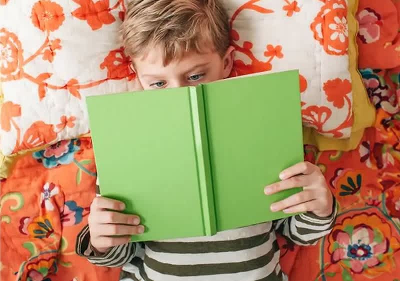 Junge liest ein Buch im Bett liegend