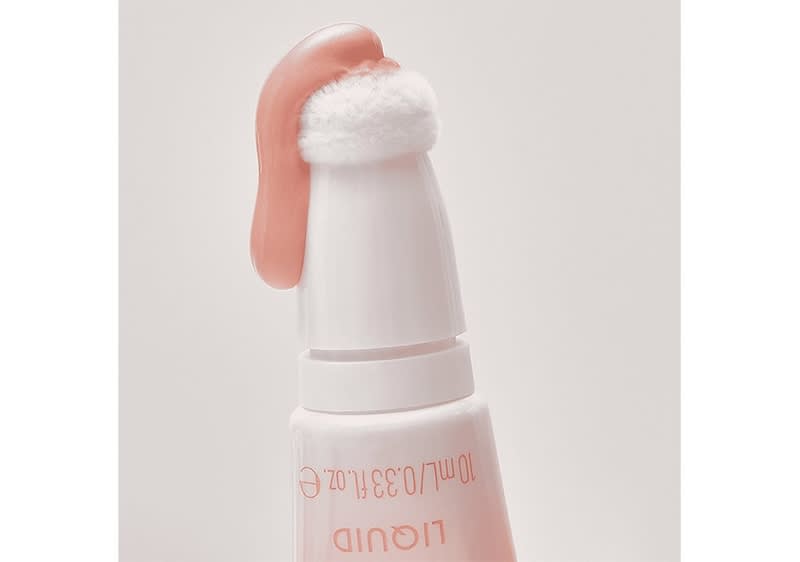 Eine weiße Flasche mit einem rosa Applikator, der mit einem weichen, weißen Schwamm bedeckt ist, auf dem rosa Flüssigkeit aufgetragen wurde; die Flasche hat die Aufschrift 10ml/0.33 fl.oz und LIQUID in rosa Schrift.