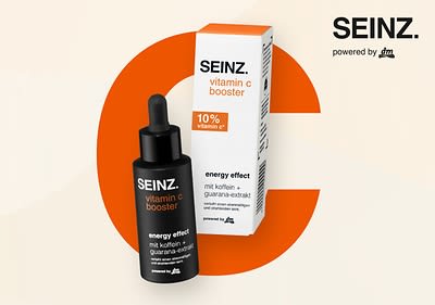 Eine Produktabbildung des SEINZ. Vitamin C Boosters mit einer schwarzen Flasche und einem weißen Etikett, auf dem SEINZ. vitamin c booster und energy effect mit koffein + guarana-extrakt steht, daneben eine weiße Verpackung mit denselben Aufschriften und einem orangefarbenen Streifen oben, auf der Verpackung steht zusätzlich 10% vitamin c*, im Hintergrund sind gelbe und orangefarbene Bläschen zu sehen, oben rechts steht groß SEINZ.