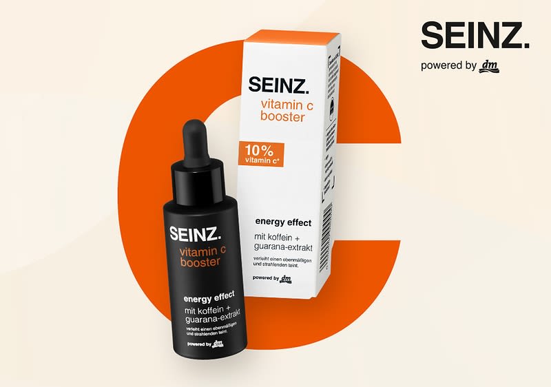 Eine Produktabbildung mit einer schwarzen Flasche und einer weißen Verpackung, beide mit der Aufschrift SEINZ. vitamin c booster, die Flasche trägt zusätzlich die Worte energy effect mit koffein + guarana-extrakt und powered by dm, die Verpackung zeigt 10% vitamin c* und energy effect mit koffein + guarana-extrakt, im Hintergrund ein großes oranges C und oben rechts der Schriftzug SEINZ. powered by dm