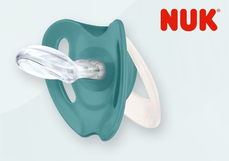 Ein türkisfarbener NUK Schnuller mit transparentem Sauger und weißem Ring, oben rechts ist das rote NUK-Logo zu sehen