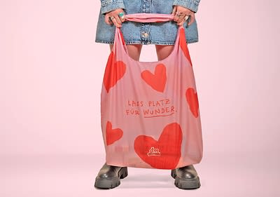 Catalin hält eine rosa Einkaufstasche mit roten Herzen und der Aufschrift „Lass Platz für Wunder“