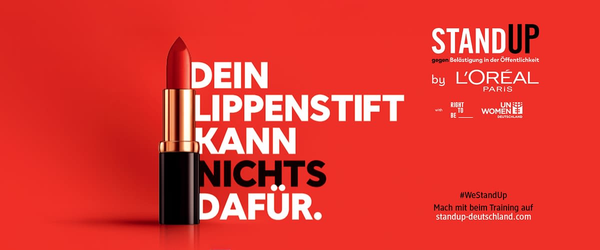 Ein roter Lippenstift vor rotem Hintergrund, daneben der Text „Dein Lippenstift kann nichts dafür“. Oben rechts steht „Stand Up gegen Belästigung in der Öffentlichkeit“ und darunter „by L'Oréal Paris“ sowie Logos von „UN Women“ und „Right To Be“. Unten rechts der Hashtag „#WeStandUp“ und der Hinweis „Mach mit beim Training auf standup-deutschland.com“