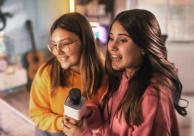 Zwei Personen in gelbem und rosa Pullover halten ein Mikrofon in einem Raum mit verschwommenem Hintergrund