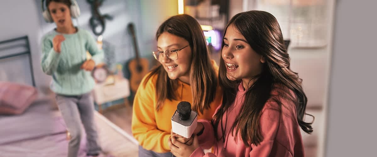 Zwei Personen in gelbem und rosa Pullover halten ein Mikrofon in einem Raum mit verschwommenem Hintergrund