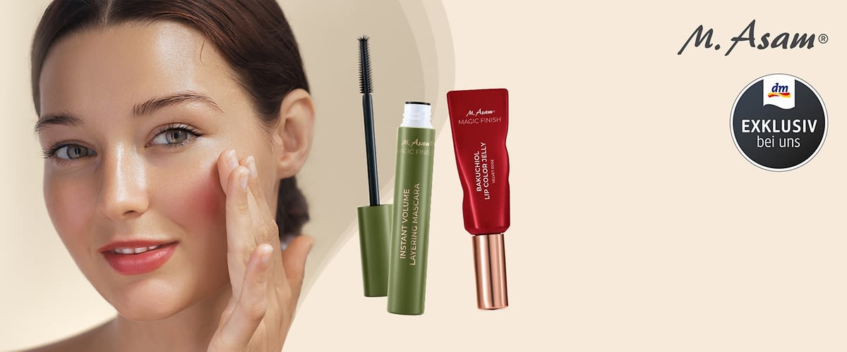 Zwei Kosmetikprodukte von M. Asam, links eine grüne Mascara mit der Aufschrift „Instant Volume Lifting Mascara“, rechts ein roter Lipgloss mit der Aufschrift „Magic Finish Balm & Color Lip Booster“, daneben das dm-Logo mit dem Text „Exklusiv bei uns“