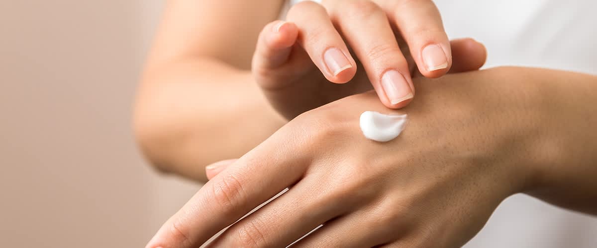 Eine Hand trägt eine kleine Menge weißer Creme auf den Handrücken auf
