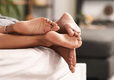 Nahaufnahme der Füße von zwei Personen, die auf einem Bett liegen. Die Fußsohlen sind sichtbar.