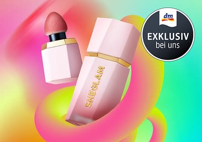 Zwei rosa SHEGLAM Kosmetikprodukte mit goldenen Akzenten vor einem bunten Hintergrund, daneben ein schwarzer Kreis mit der Aufschrift „EXKLUSIV bei uns“ und dem dm-Logo