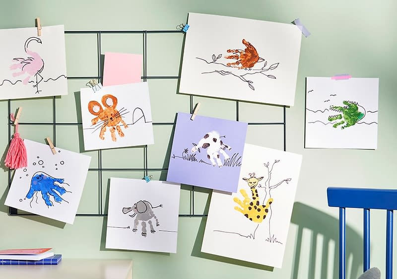 Mehrere Kinderzeichnungen hängen an einem Gitter, darunter ein rosa Flamingo, ein orangefarbener Oktopus, ein brauner Affe, eine grüne Krokodilfigur, ein blauer Fisch, ein grauer Elefant und eine gelbe Giraffe