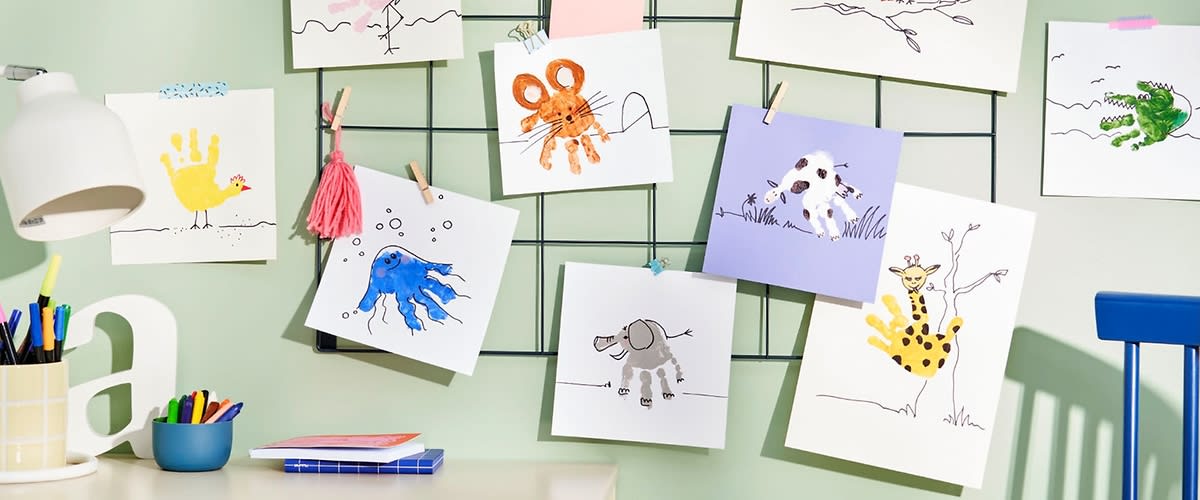 Mehrere Kinderzeichnungen hängen an einem Gitter, darunter ein rosa Flamingo, ein orangefarbener Oktopus, ein brauner Affe, eine grüne Krokodilfigur, ein blauer Fisch, ein grauer Elefant und eine gelbe Giraffe