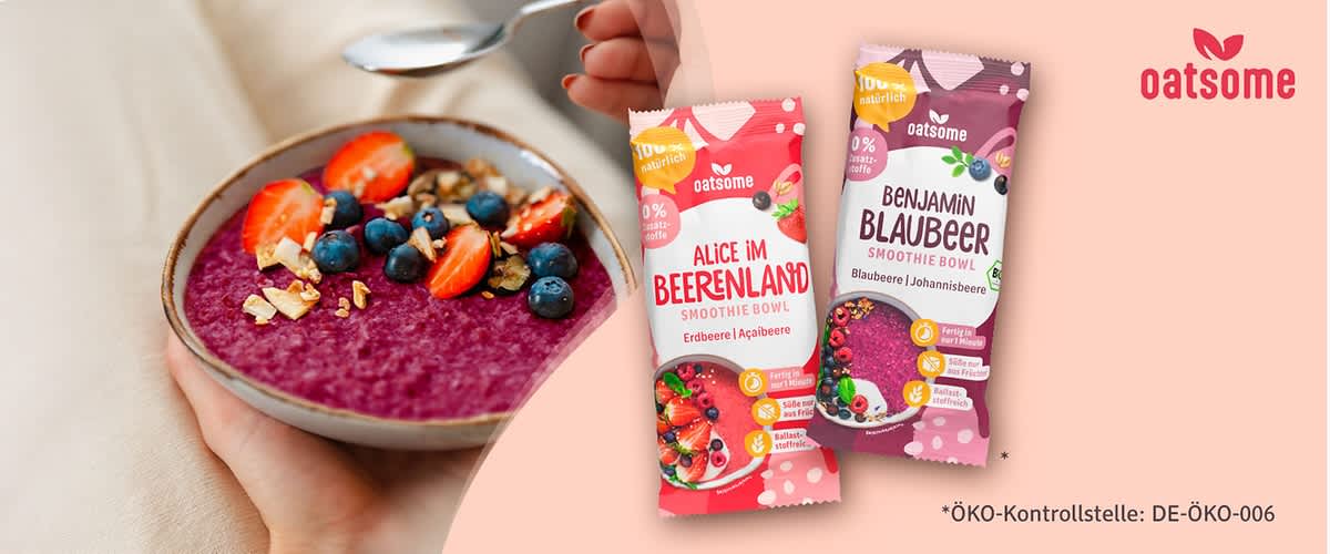 Zwei Smoothie Bowl Verpackungen von oatsome, links „Alice im Beerenland“ mit Erdbeere und Açai, rechts „Benjamin Blaubeer“ mit Blaubeere und Johannisbeere, daneben eine Hand hält eine Schüssel mit einer roten Smoothie Bowl, garniert mit Erdbeeren, Blaubeeren und Müsli