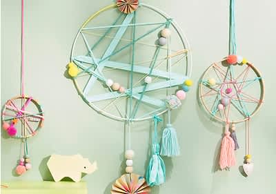 Zwei dekorative Traumfänger aus bunten Fäden und Perlen hängen an einer mintgrünen Wand, daneben ein gelbes Nashorn aus Holz auf einem Regal