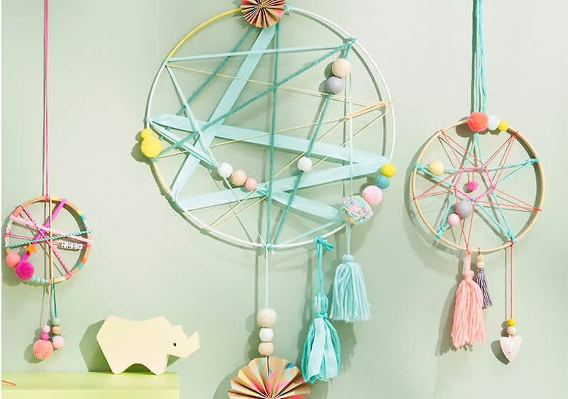 Zwei dekorative Traumfänger aus bunten Fäden und Perlen hängen an einer mintgrünen Wand, daneben ein gelbes Nashorn aus Holz auf einem Regal