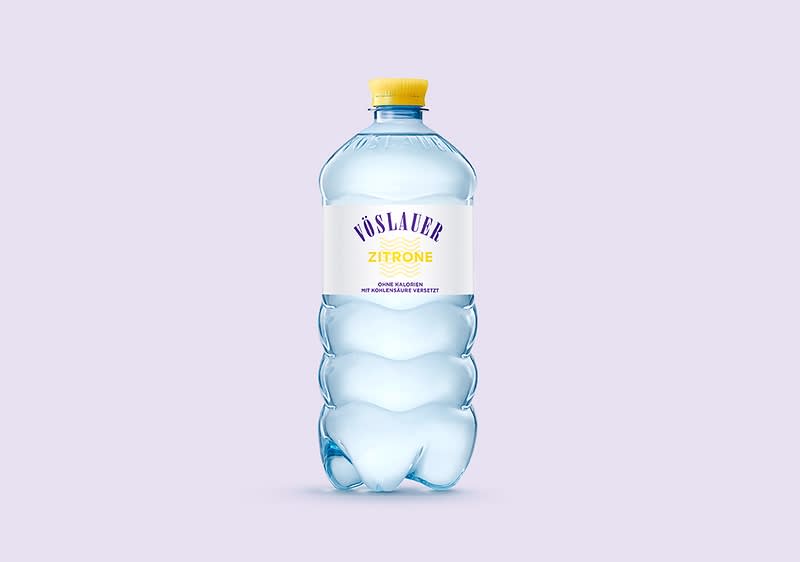 Eine blaue Plastikflasche mit gelbem Deckel, darauf die Aufschrift „Vöslauer Zitrone“ in lila und gelb, darunter „Natürliches Mineralwasser“