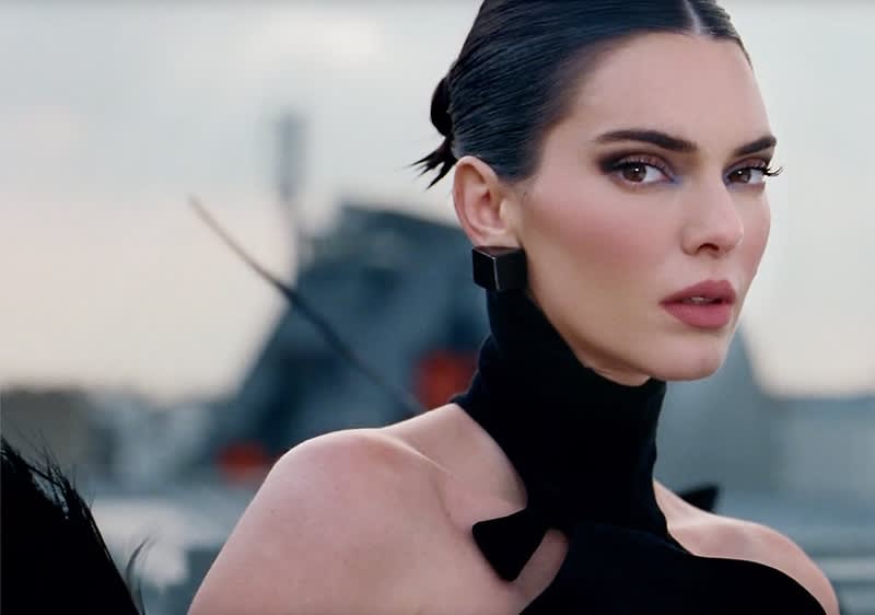 Eine Person trägt ein schwarzes, elegantes Kleid mit hohem Kragen und Schleifendetail auf der Schulter