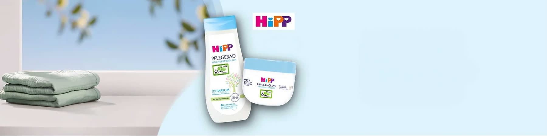 Eine weiße Flasche Pflegebad und eine weiße Dose Familiencreme der Marke HiPP, beide mit blauen Deckeln und der Aufschrift „Hochverträglich“